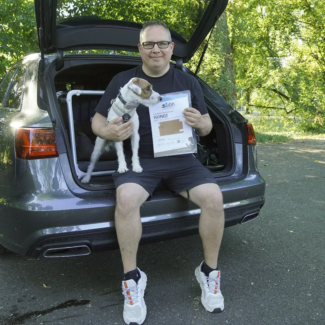 Teilnehmer mit kleinem Hund und Prüfungsurkunde am Auto